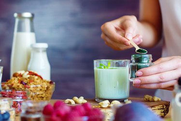 person adding spirulina powder, one of the plant-based protein foods, to drink