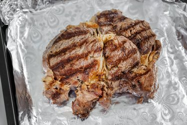 Close-up tasty juicy rib eye steak on aluminium foil. . Organic beef meat seasoned with ground pepper coocked in oven after grill