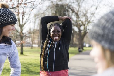 Smiling female runner stretching in sunny park