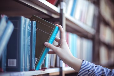 Hand of person selecting a book from book shelf