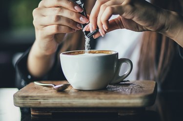hand pouring packet of sugar into her coffee on wooden table