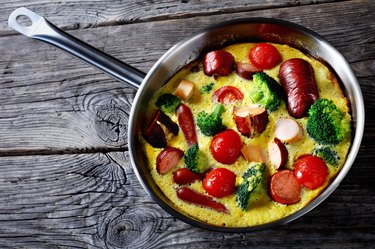 baked omelet or frittata with sausages, broccoli, cherry tomatoes, melted cheese in a skillet