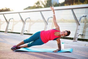Smiling woman doing side plank while finishing workout