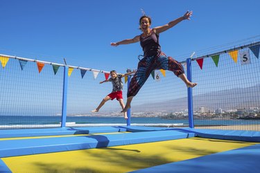 Playful mother and son bouncing on trampoline at the coast