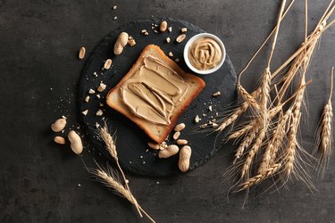 Slate plate with tasty toast and peanut butter on table