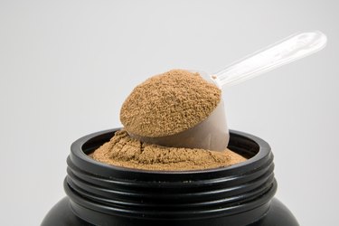 A cup of whey protein powder for muscle gains or diet person is in a plastic bottle on white background