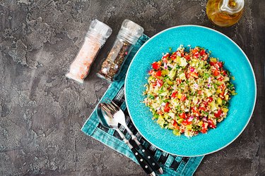 Salad with quinoa, arugula, sweet peppers, tomatoes and cucumber in bowl on a dark background. Healthy food, diet, detox and vegetarian concept. Tabbouleh salad. Top view. Flat lay