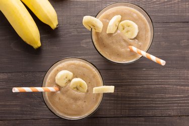 Banana smoothie and fresh banana on wooden background