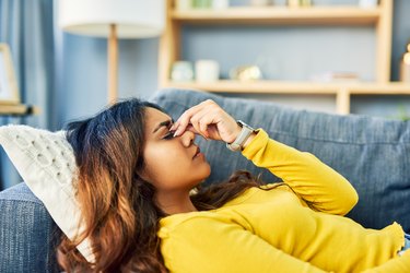 woman wearing yellow sweater lying down on couch holding head with headache