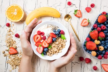 Women's hands holding granola with berries, fruits, yoghurt and coffee for breakfast. Cereal oats with strawberries, blueberries and raspberries for healthy eating. Top view