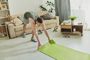 a person rolls out a light green yoga mat on the floor to do stress-reducing yoga exercises at home