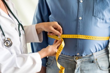 A doctor measuring a man's waist to determine if his body fat percentage is considered obese