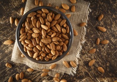 overhead shot of raw Protein-rich Almonds in a bowl on wooden table