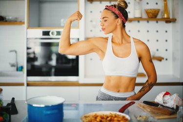 Woman in gym clothes flexing in kitchen