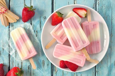 Healthy summer strawberry yogurt popsicles, top view table scene against blue wood