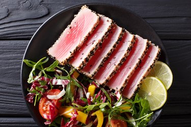 Top view of seared tuna steak, sliced and served with lime and a fresh salad