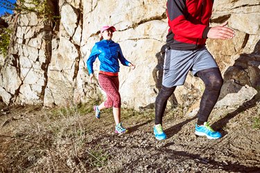 The guy and the girl are running along the path in the mountains.