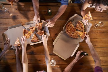 Overhead shot of friends at a table sharing take-away pizzas