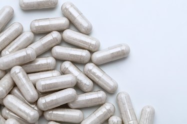 Pile of capsules with probiotic powder inside on white background.