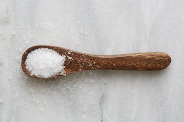 Overhead view of a wooden spoon filled with Celtic sea salt on a white marble countertop