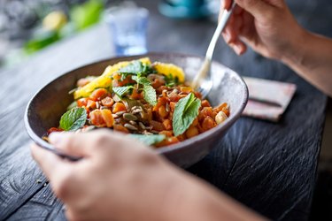 Healthy person eating organic chickpea salad from bowl with fork at rustic bohemian restaurant