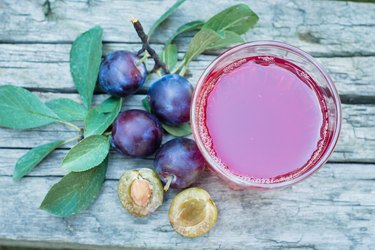 Plum juice in glass on wooden table background. Natural Green Leaf Background. Copy space