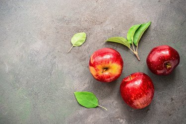 Three ripe bright red apples with green leaves on a rustic textured background, top view. Copy space