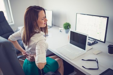 A woman sitting at her desk and holding her back in pain