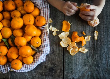 Cropped Hands Peeling Oranges On Wooden Table