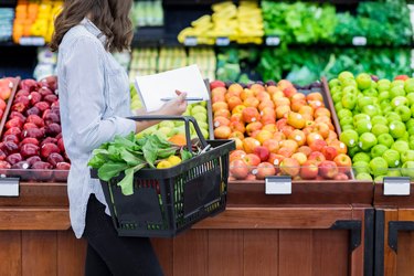 An unrecognizable person shops for produce in the supermarket and calculates how many points are in an apple and medium sweet potato weight