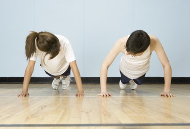 Teenage boy and girl (12-14) doing push-ups side by side in gymnasium