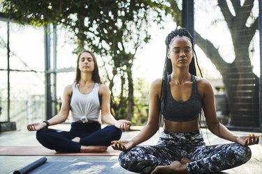 Young woman practicing lotus position with friend at a yoga class