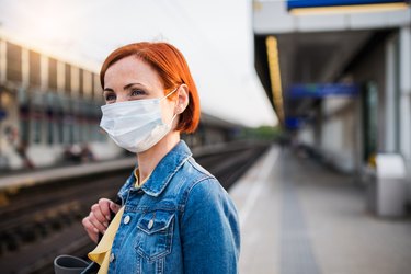 Portrait of young woman wearing protective face mask outdoors in city, waiting for the train.