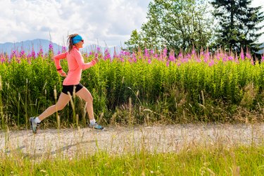 Young woman running on country road in mountains, summer day