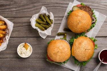 different hamburger on wooden table with sauces, fries and pickl