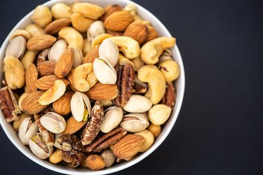 an overhead photo of a white bowl of mixed nuts on a black background