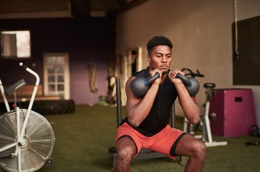 Man in a CrossFit gym using two kettlebells as free weights to do squats