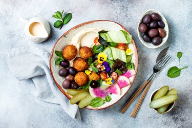 Middle eastern lunch Buddha bowl with hummus, falafel, tomato and greens salad, olives, pickles and edible flowers