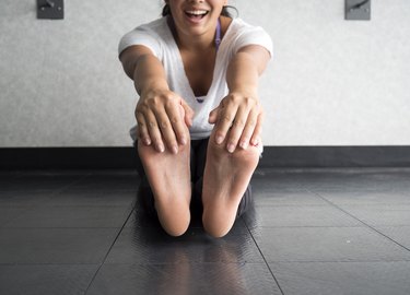 Smiling woman grabbing her feet to stretch hamstrings