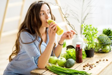 A woman drinking a green juice, surrounded by green food