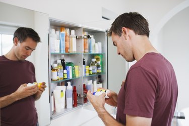 Man looking at bottles of over-the-counter pill bottles from medicine cabinet with reflection in mirror