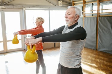 Senior couple in gym working out using kettle bells