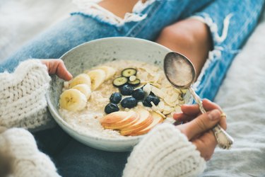 Person in jeans and sweater eating healthy oatmeal porridge