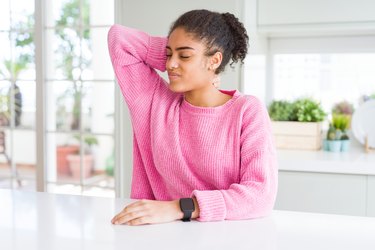 black woman in a pink sweater rubbing her neck before doing exercises for neck pain