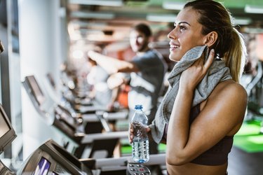 Happy athletic woman cleaning sweat during water break on a treadmill in a gym.