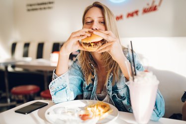 a woman eating a burger in a restaurant, as an example of foods that cause body odor