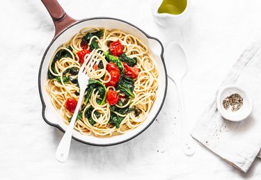 Whole grain spaghetti pasta with cherry tomatoes and spinach sauce in a cast iron pan on a white background, top view. Copy space, healthy diet food concept