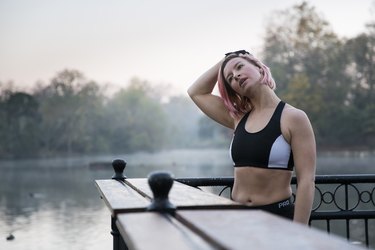 Woman stretching neck while standing by lake at park
