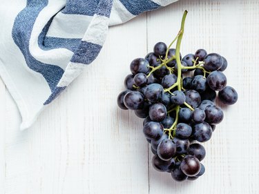 Dark vitamin K-rich grape bunch on white wooden table