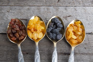 Different colored raisins in metal spoons on wooden table